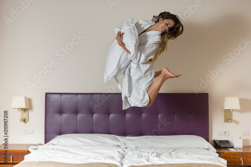 Funny young woman jumping on white bed