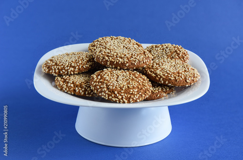 Oatmeal cookies with sesame seeds in a white dish on a violet ba photo