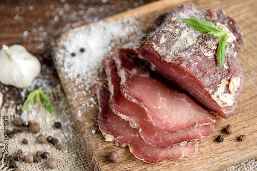 Pork dried meat slices on rustic dark wooden background. Dried pork prosciutto salami ham with herbs.