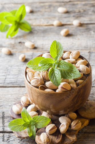 Delicious salted pistachios and fresh mint leaves on wooden background