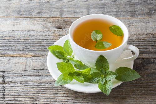 Cup of tea with fresh mint leaves on wooden background. Copy space