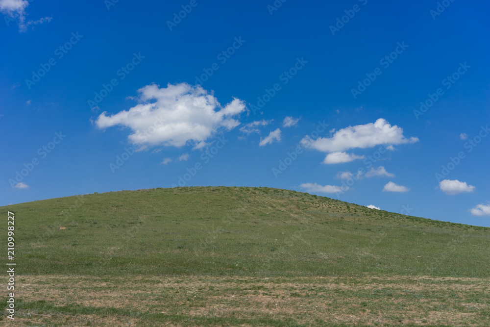 Green hill covered with grass against a blue sky with clouds. Green hill covered with grass against a blue sky with clouds.