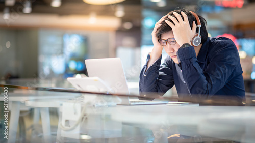 Young Asian business man feeling stressed and frustrated while working with laptop computer. Male entrepreneur getting in trouble with his job. freelance lifestyle in urban workspace.