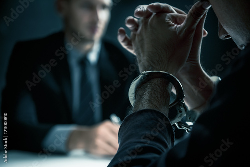 Criminal man with handcuffs in interrogation room photo