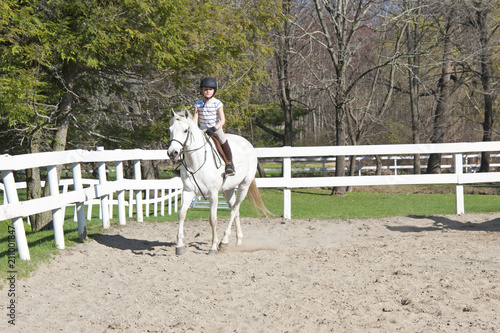 Young girl on white horse at horseback riding lesson. 