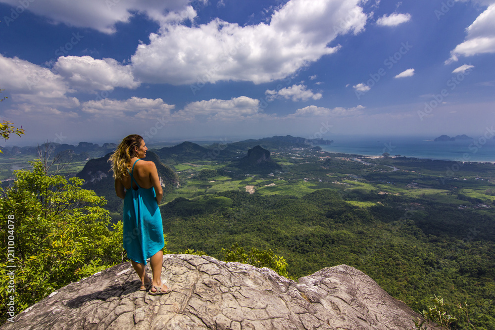 Naklejka premium girl with hands up standing on rock at sunset with mountains below