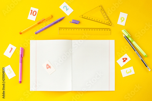 Notebook in the cell among pens, pencils, numbers and rulers on a yellow background. Accessories for study. Mathematics, geometry, algebra. Top view, flat lay