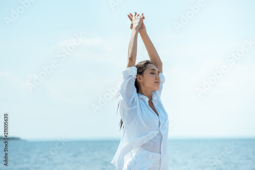 young asian woman with closed eyes standing with wide arms in front of sea