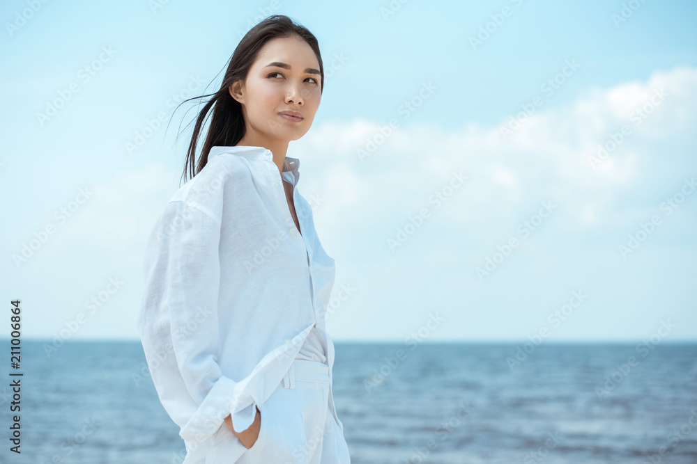 young asian woman with hands in pockets looking away by sea young asian woman with hands in pockets looking away by sea