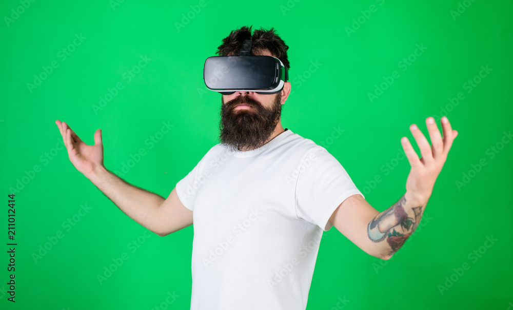 Superiority concept. Hipster on serious face raising hands while enjoy superiority in virtual reality. Guy with head mounted display interact in VR. Man with beard in VR glasses, green background