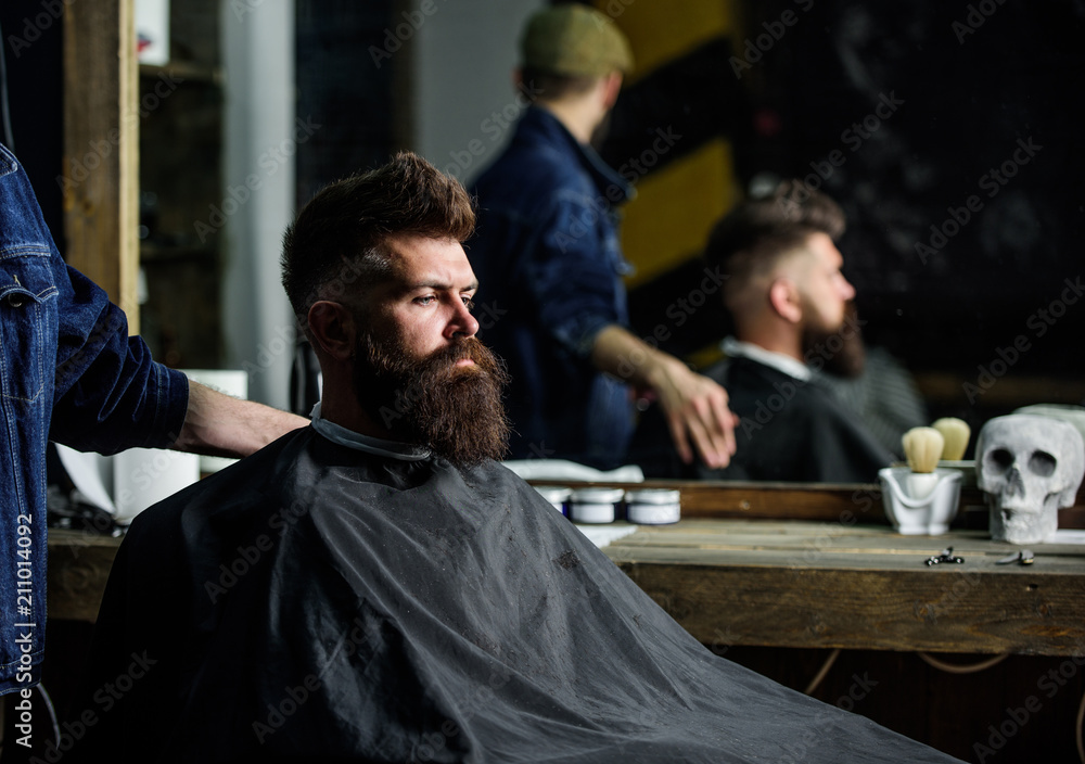 Premium Photo  A bearded man sitting in an armchair and having a barber  fix a cape around him