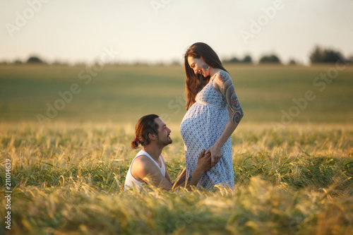 Счастливый молодой мужчина и счастливая, молодая, беременная женщина на закате в пшеничном поле