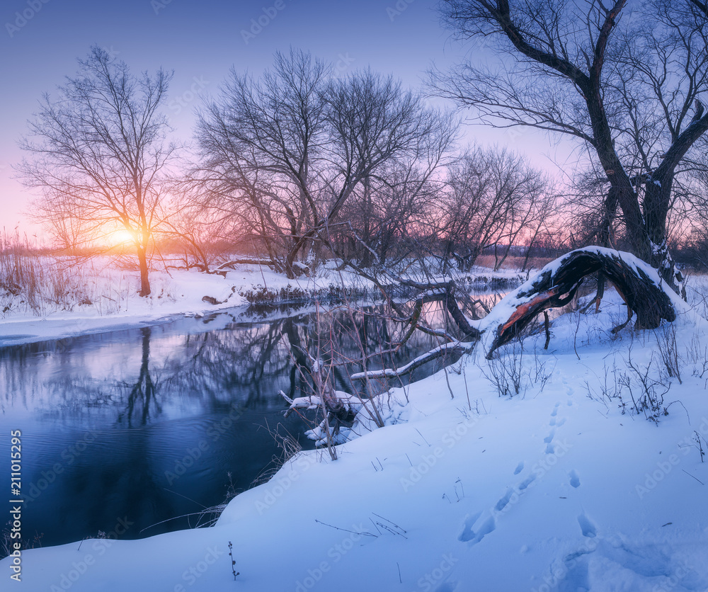Winter forest and river at sunset. Colorful landscape with river with reflection in water in cold evening. Forest, lake, sun and purple sky. Beautiful winter. Christmas background. Nature Photo