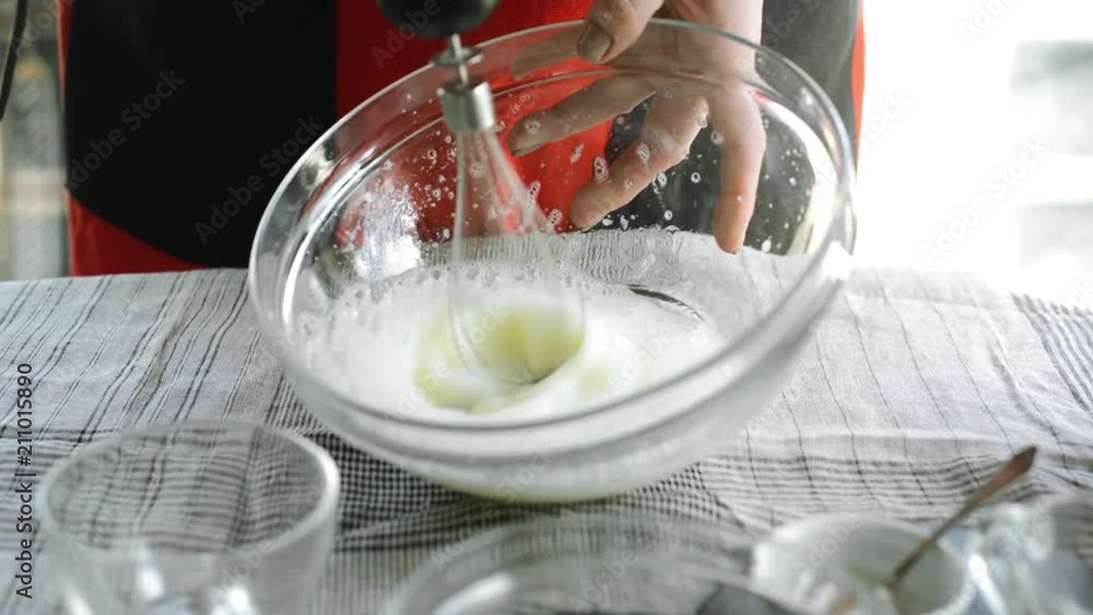 Closeup woman whip egg white in glass bowl by mixer Closeup woman whip egg white in glass bowl by mixer