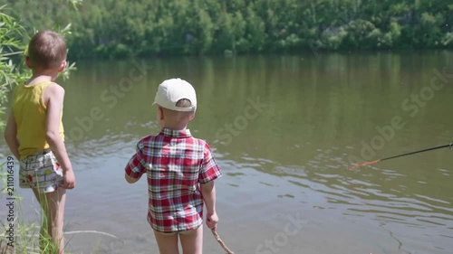 Two children stand on the river Bank. In the hands of children rods. Hot summer day. photo