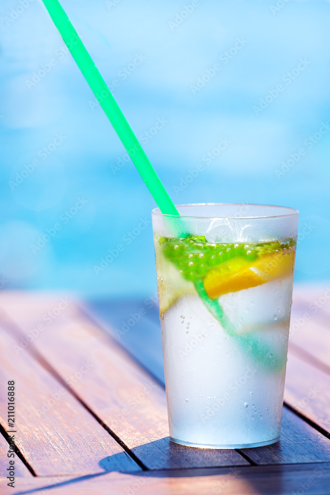 Mojito cocktail with lime and mint in highball glass on wooden table near pool. Mojito cocktail with lime and mint in highball glass on wooden table near pool.