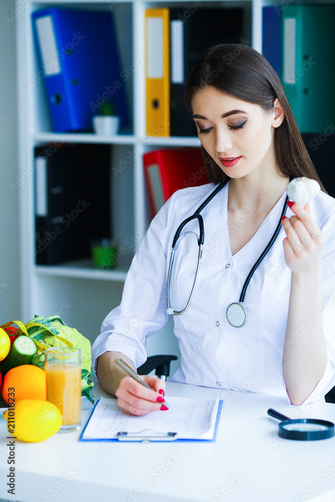 Health. Diet and Healthy. Nutrition. Portrait of a Dietitian's Doctor with Fresh Fruits and Vegetables. Beautiful and Young Doctor in the Light Room Holding in Garlic Hands. High Resolution Health. Diet and Healthy. Nutrition. Portrait of a Dietitian's Doctor with Fresh Fruits and Vegetables. Beautiful and Young Doctor in the Light Room Holding in Garlic Hands. High Resolution