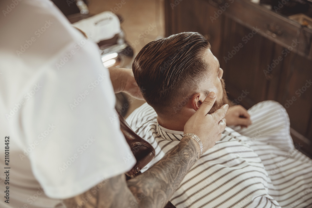Barber lubricates the client's beard with oil. Photo in vintage style Barber lubricates the client's beard with oil. Photo in vintage style