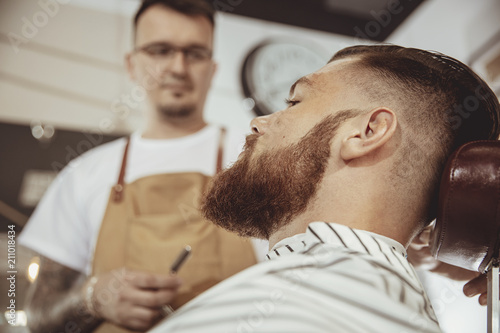 Man with beard waits for a shave with a razor in a barbershop. Photo in vintage style