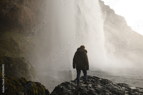 Man wearing a coat under a waterfall in iceland in winter