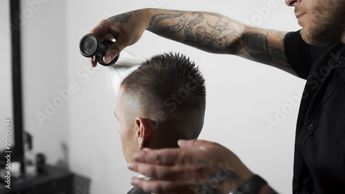 Barber whisks away sheared hairs from customer's shoulders by brush, tattoed barber makes haircut for customer at the barber shop, man's haircut and shaving at the hairdresser photo