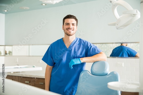 Portrait Of Smiling Dentist Standing By Chair At Clinic