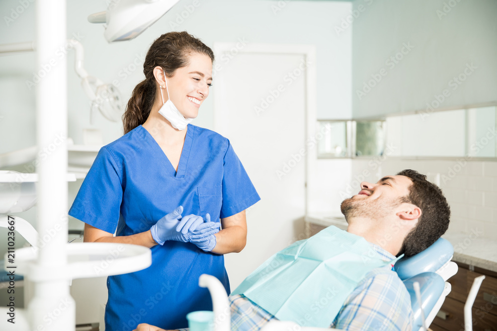 Obraz premium Smiling Dentist In Scrubs Talking To Patient At Clinic