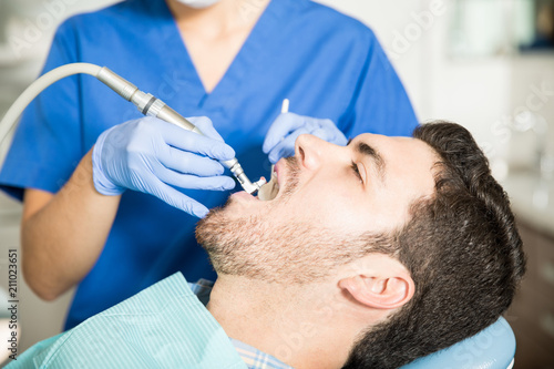Man Receiving Dental Treatment From Dentist In Clinic