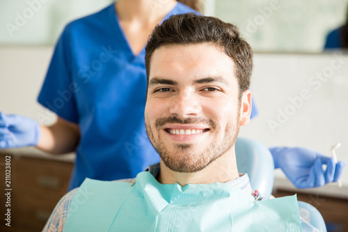 Smiling Man With Dentist Holding Dental Tools At Clinic