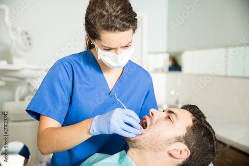 Dentist Examining Man With Dental Carver At Clinic