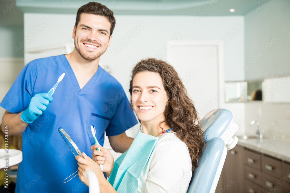 Fototapeta premium Smiling Dentist And Woman Holding Toothbrushes In Dental Clinic