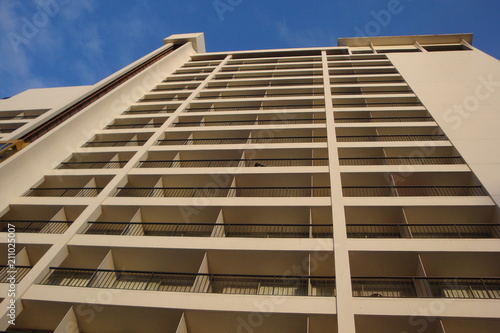 Upward view of a tall apartment building with beige stonework and blue sky