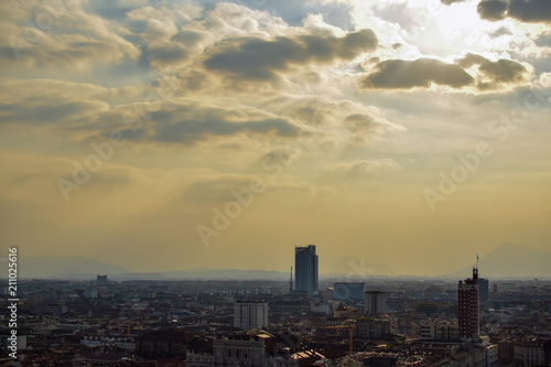 View of the whole of a city from the heights seeing the streets and squares in perspective next to the clouds and some rays of sun that cross them. Photograph taken in Turin, Italy.