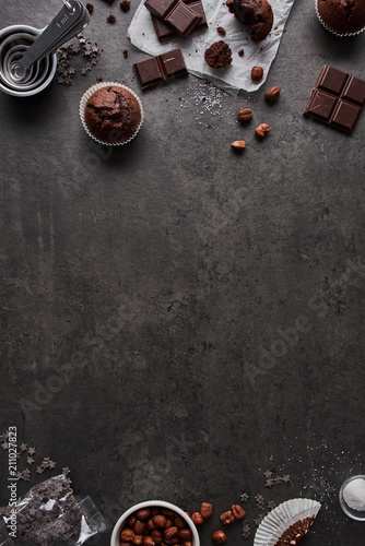 Baking background with chocolate muffins, measuring cups, chocolate, sugar and nuts on dark concrete background. Flat lay with copy space in the middle. photo