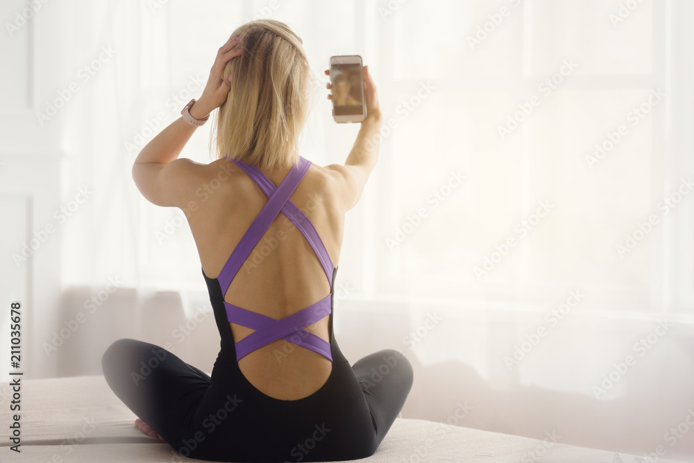 Back view of fit slim woman doing selfie in front of window Back view of fit slim woman doing selfie in front of window