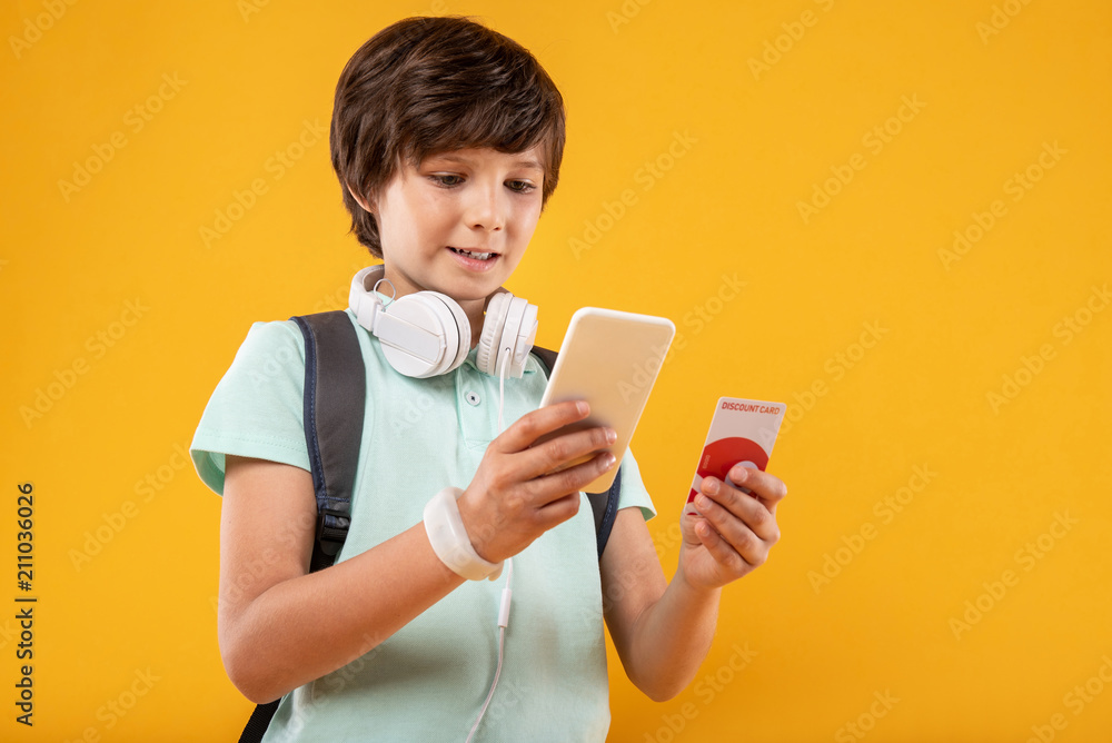 Incredible device. Joyful dark-haired boy smiling and holding his advanced phone Incredible device. Joyful dark-haired boy smiling and holding his advanced phone