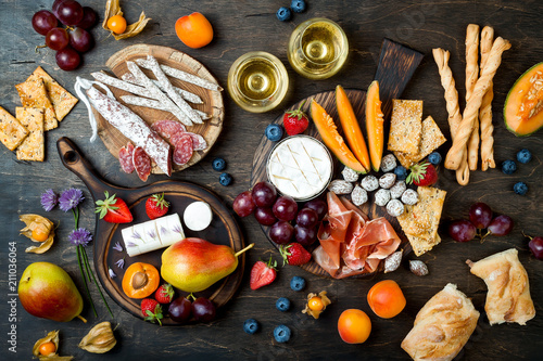 Appetizers table with italian antipasti snacks and wine in glasses. Cheese and charcuterie variety board over rustic wooden background