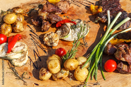 Grilled meat with grilled vegetables and spices on a wooden table.