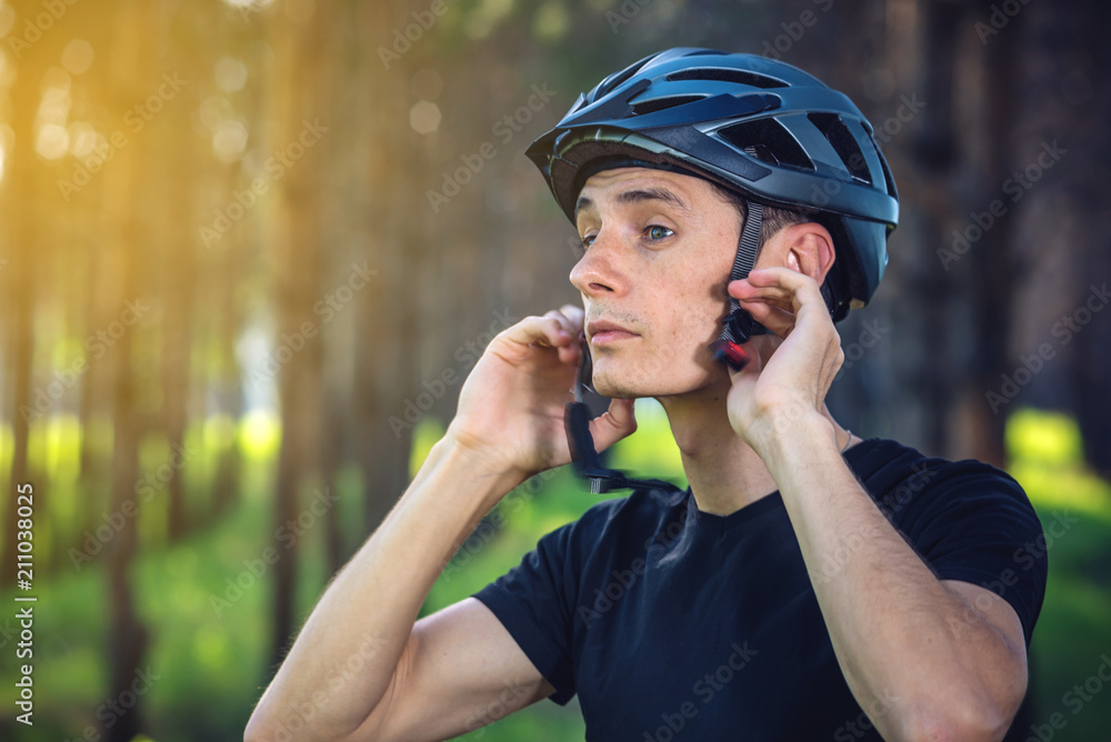 Cyclist is wearing a sports helmet on his head in the background of green nature. Protection during Cycling