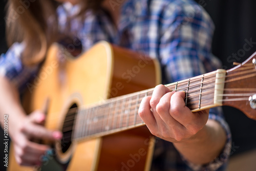 Girl playing an acoustic guitar on a dark background in the Studio. Concert young musicians. Close up.