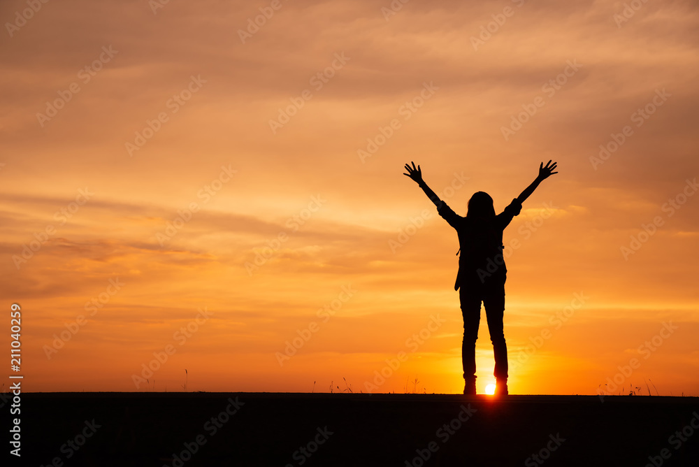 Silhouette of backpacker,person back view standing with raised hand in successful job.Asian lonely woman with sunset background in Thailand.Travel and success concept.