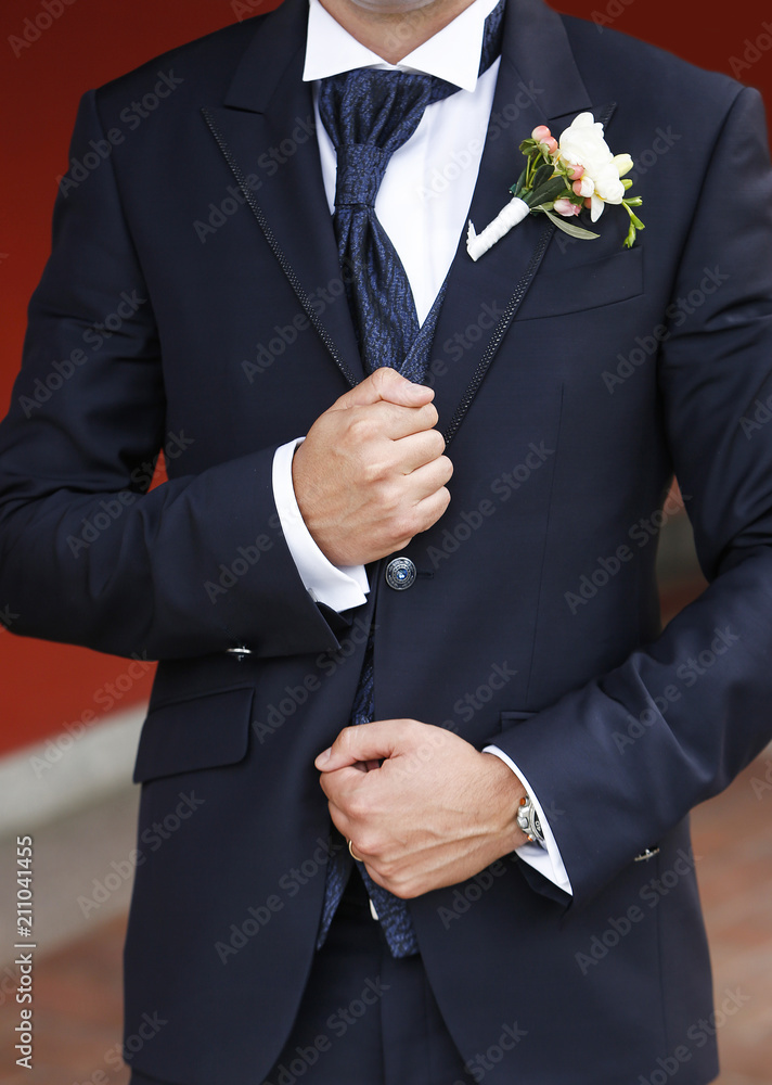 Dettaglio abito da sposo con camicia bianca, giacca blu, cravatta blu, e  mani dello sposo che tengono un bottone Photos | Adobe Stock
