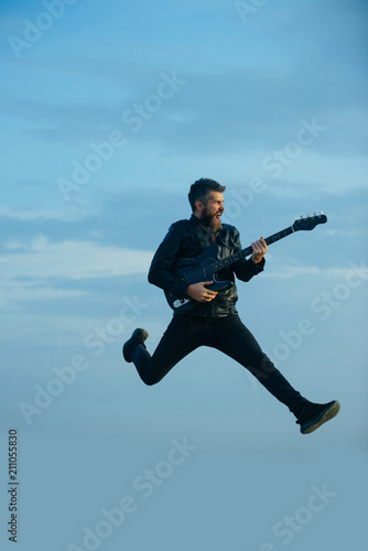 Music is so much fun. Bearded man jump with guitar on blue sky. Hipster guitarist with beard on excited face play in clouds. Like rock star. Feeling free and happy. I love my guitar