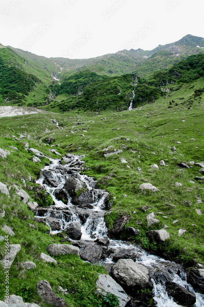 Mountain river with a waterfall among green grass and stones in Romania, Transfagarasan