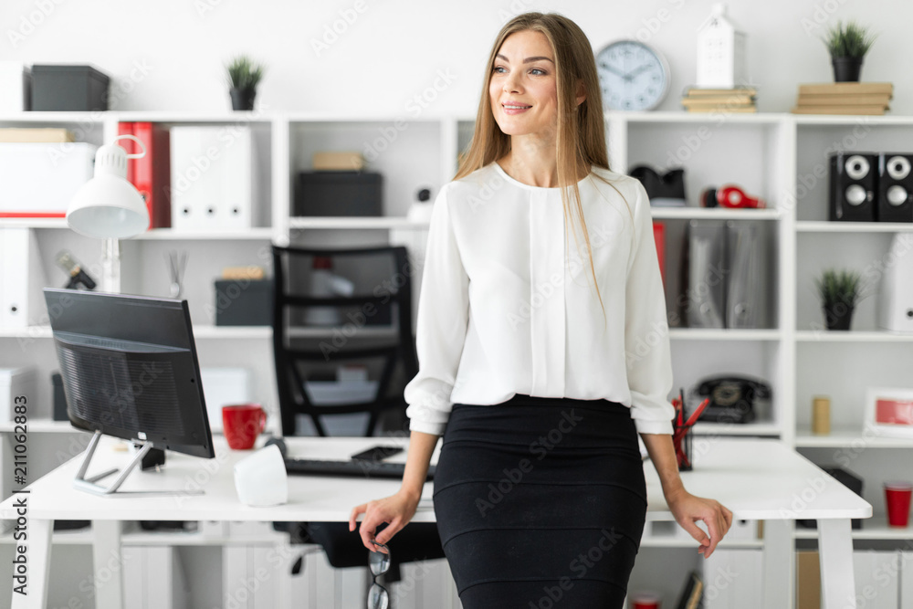 A young girl is standing leaning on a table in the office and holding glasses in her hand. A young girl is standing leaning on a table in the office and holding glasses in her hand.
