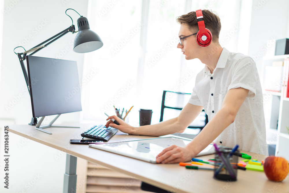A young man with glasses and headphones is working at the computer. Before the guy is a magnetic board and markers.