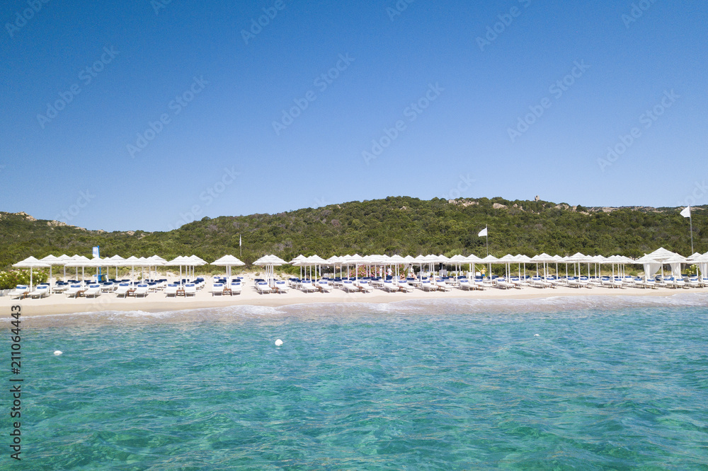 Aerial view of amazing seaside resort with white umbrellas and sun loungers. Beautiful sunny summer day in Sardinia, Mediterranean sea, Italy..