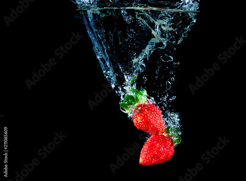 Red strawberry dropped into the water with splash on a black background