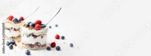 Two jars with tasty parfaits made of granola, berries and yogurt on white wooden table. Shot at angle with place for text, banner.