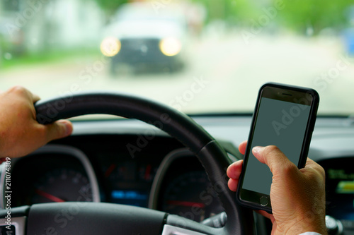 Don't text and drive ! A man is texting with a finger while a car is arriving in front.  focus on the finger, focus on telephone, focus on the car coming.